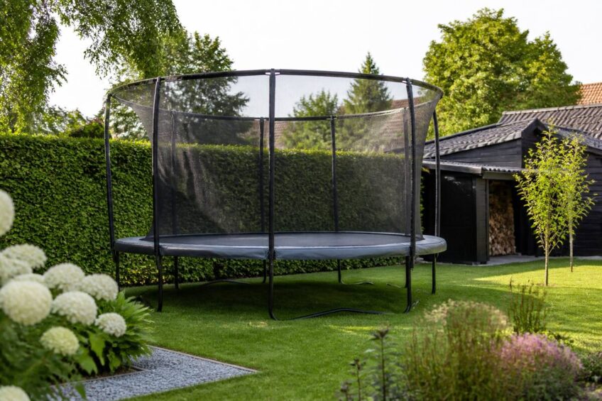 Trampoline met veiligheidsnet in een verzorgde tuin