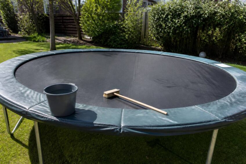 Trampoline in de tuin die wordt schoongemaakt met borstel en emmer