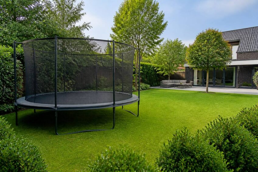 Ronde trampoline met veiligheidsnet in een nette achtertuin